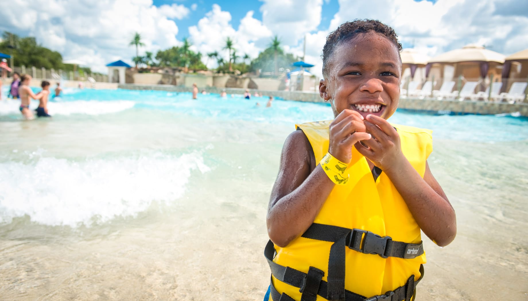 wavepool-boy Boy in a yellow life jacket smiling and enjoying Splashway's Wavepool.