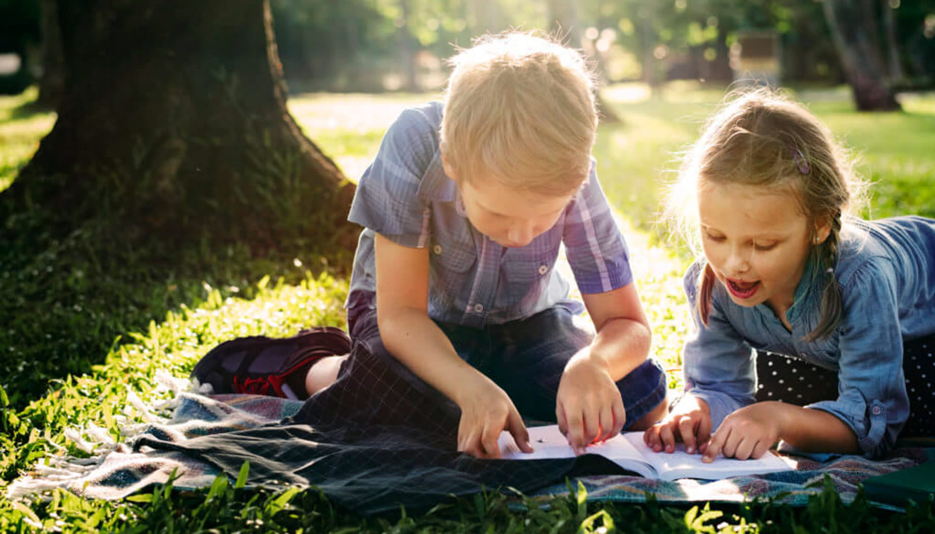 playing-in-park Two children lie on a blanket outside, focused on a book.
